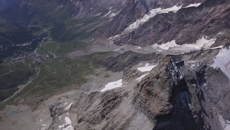 Aerial-view-from-drone-looking-into-green-valley-far-below-grey-rocky-terrain-of-Mount-Cervino-on-way-to-Matterhorn