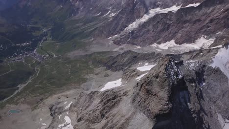 vista aérea desde un dron que mira hacia el valle verde muy por debajo del terreno rocoso gris del monte cervino en camino a la materia