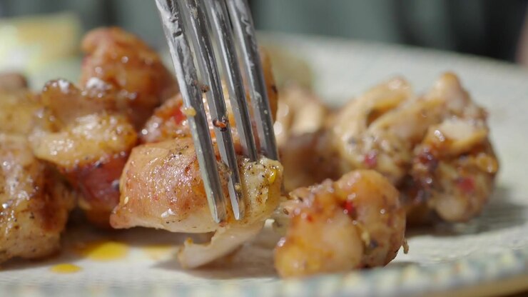 Primo piano di pezzi di pollo alla griglia mangiati con forchetta e coltello