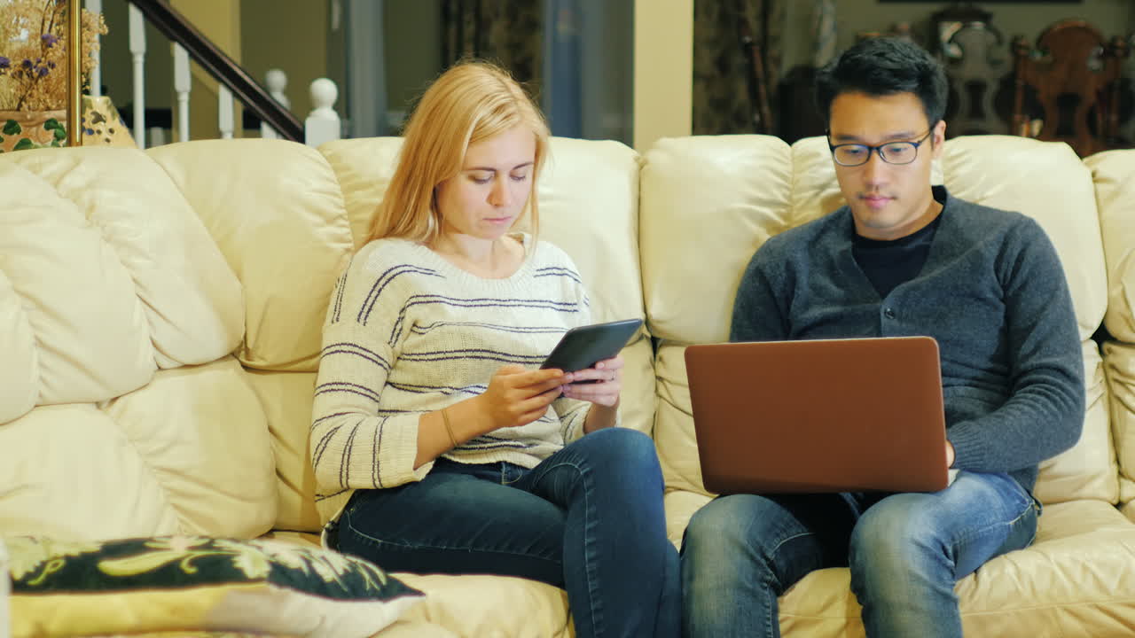 A Young Couple Sitting On The Couch Using A Laptop 2