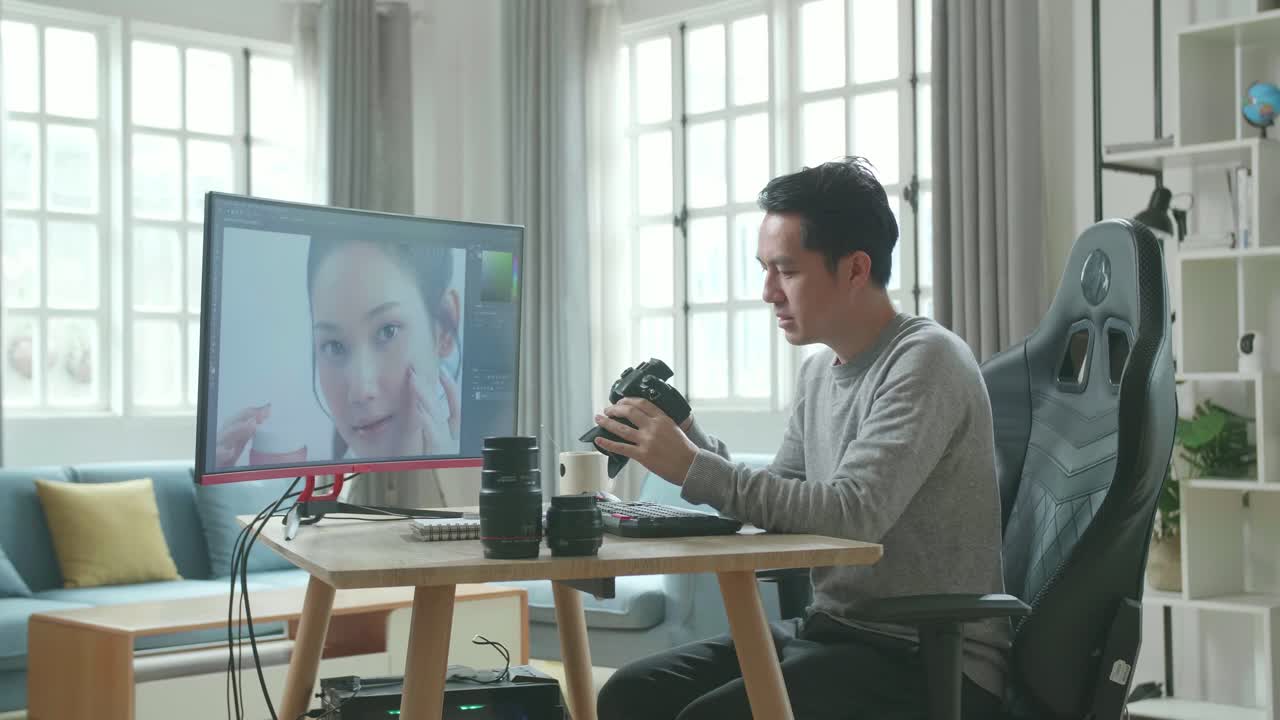 アジアのカメラマンが長袖のtシャツと黒いズボンを着てデスクトップコンピュータを使って自宅で写真を編集しながらカメラを握って見ています