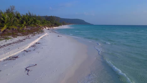 a pristine beach with palm trees meeting the crystal clear turquoise water on koh rong island, cambodia. magic aerial view flight overflight flyover drone