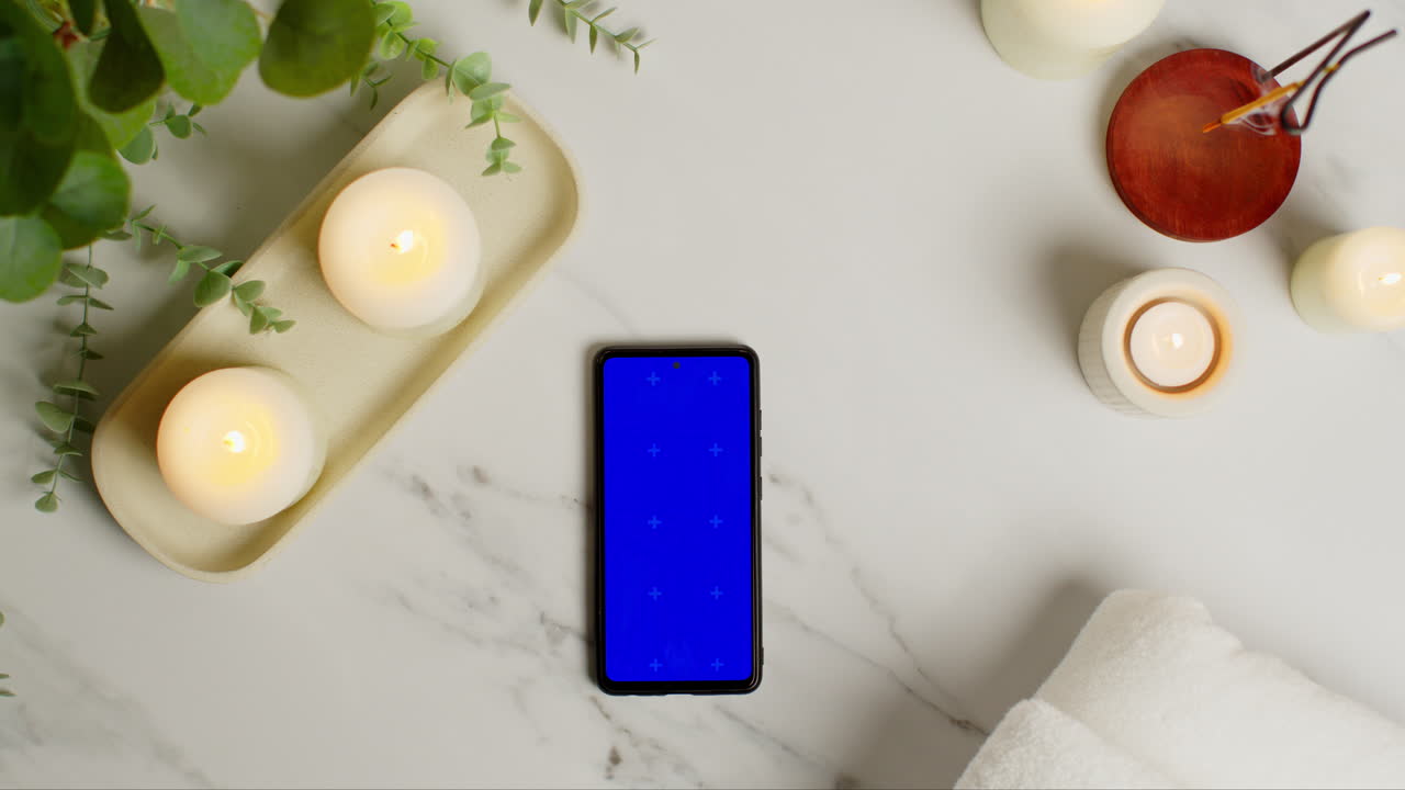 vista aérea mirando hacia abajo en la naturaleza muerta de la pantalla azul teléfono móvil encendido velas y incienso palo con planta verde y toallas como parte de la decoración del día de spa 3