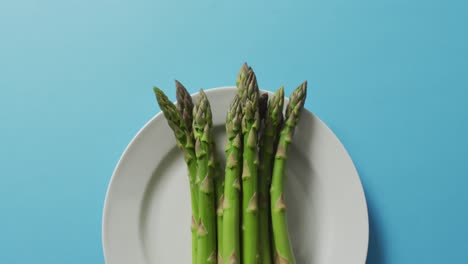 video of fresh asparagus on white plate over blue background