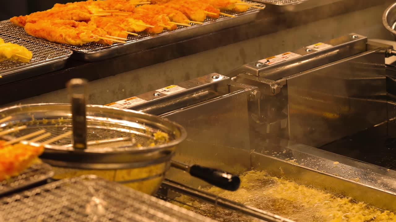 Close-up of crispy tempura resting on metal racks beside a deep fryer in a kitchen.