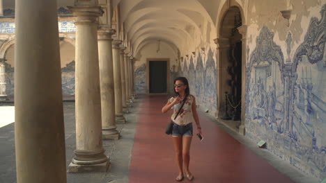 girl wearing sunglasses and holding a smartphone walks through a monastery with columns and wall paintings in salvador de bahia, a unesco world heritage site, in brazil.