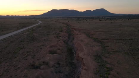 Flyover-dry-creek-outback,-Mountain-range-Silhouette-in-Distance,-Aerial-Forward