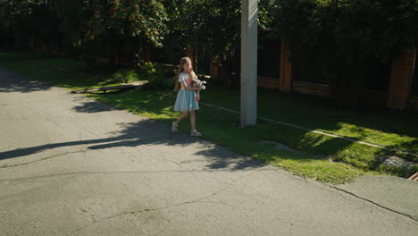 young girl holding stuffed animal walks alone on cracked suburban road bordered by greenery and fence, with sunlight casting shadows across pavement near utility pole and residential lawn