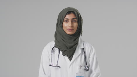 Studio-Portrait-Of-Serious-Female-Doctor-With-Headscarf-Wearing-White-Coat-Against-Plain-Background