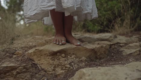 a woman in white dress is walking barefood in the forrest