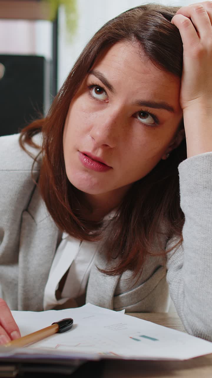 Exhausted business woman looking at documents reports stacks of books while working hard at office