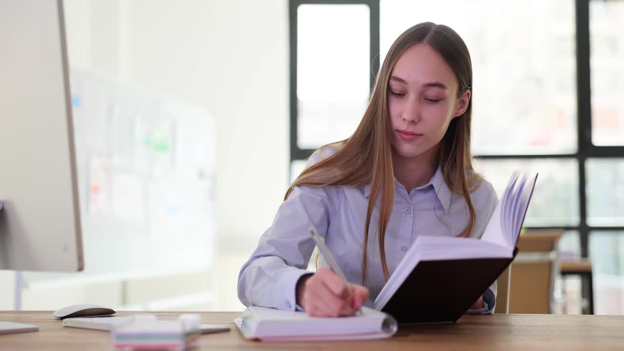 Young Woman Working on Computer and Taking Notes in an Office Setting