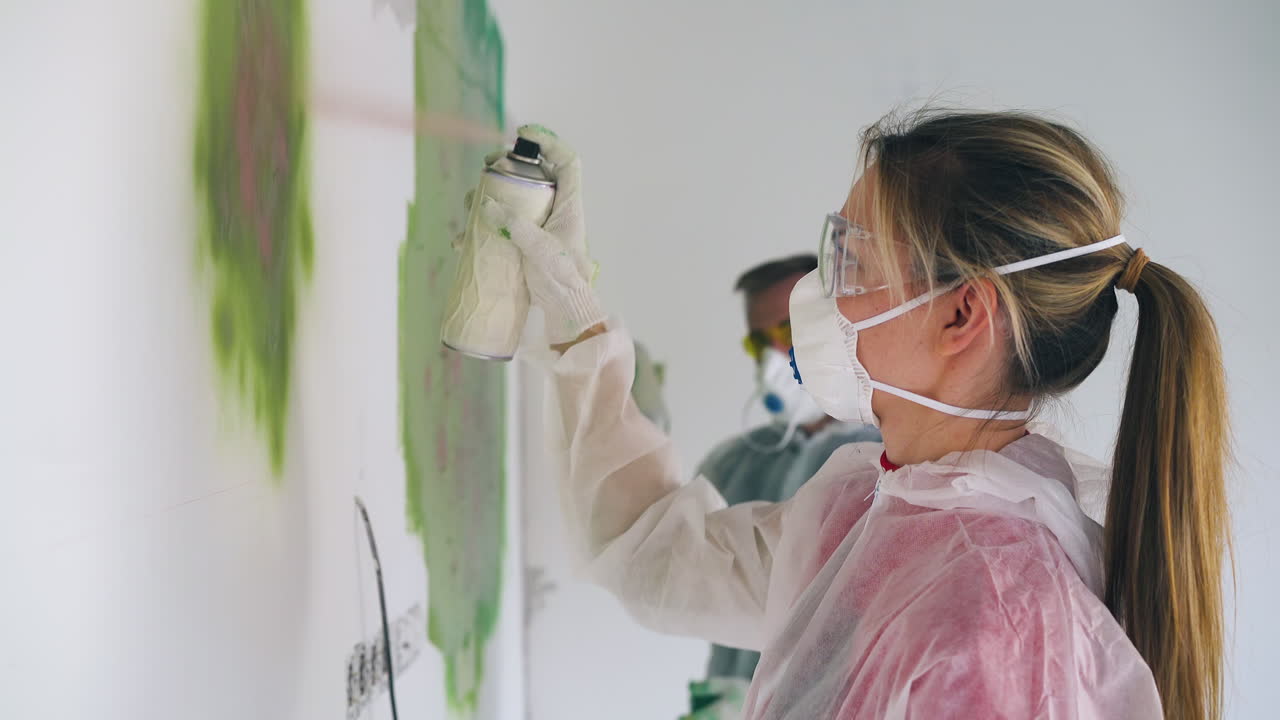 작업복을 입은 소녀와 남자친구가 녹색 스프레이로 벽을 칠합니다.