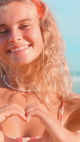 smiling girl making heart shape at the beach under clear sky