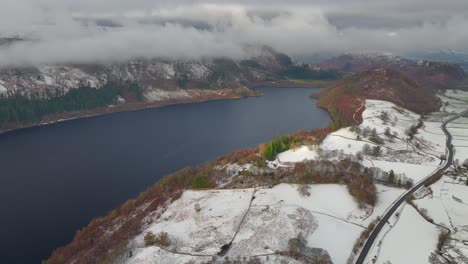 paisaje de lago oscuro y nieve ligera con montañas y trébol de nubes bajas y carretera con tráfico muy ligero