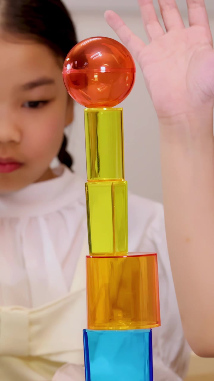 Dua anak menumpuk bersama balok magnet transparan menjadi menara tinggi di pencahayaan ruang kelas yang terang.