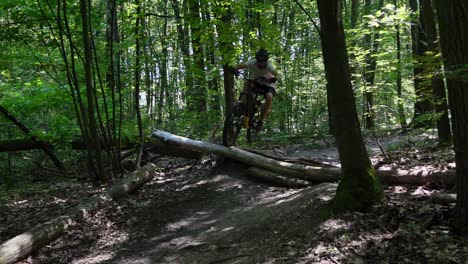 static shot of an adult male riding a bicycle in the mountains in the forest with steep corners and jumps over logs on an electric bicycle in slow motion