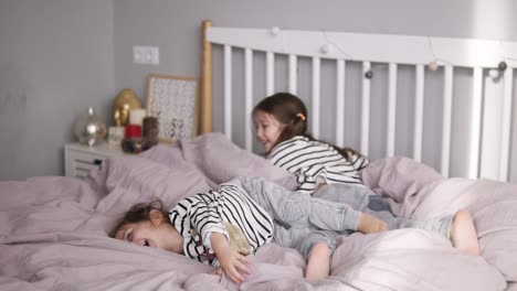 happy cute daughter with sister and mother have pillows fight lying on a pink bed and have fun in cozy light bedroom. slow motion