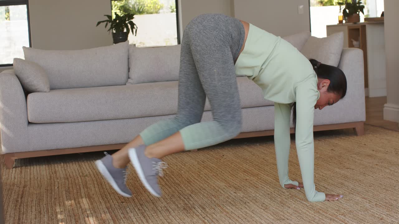 Entering high plank near beige sofa, woman performing knee drives and holding plank engaging core