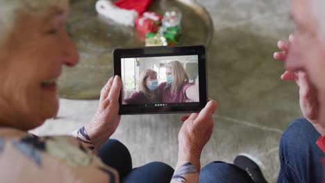 Pareja-Caucásica-Mayor-Sonriendo-Y-Usando-Una-Tableta-Para-Una-Videollamada-Navideña-Con-La-Familia-En-La-Pantalla