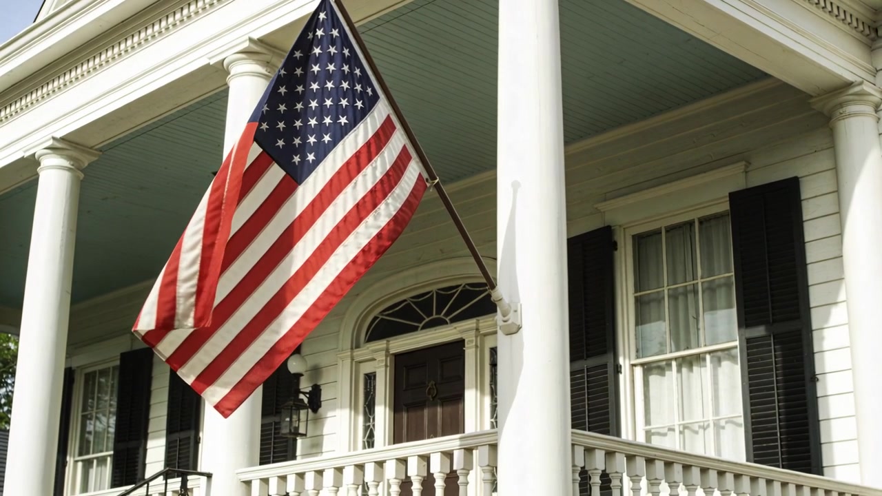 Bandiera americana che sventola al vento su un portico, vicino a colonne bianche e una staffa, mostrando le stelle e strisce.