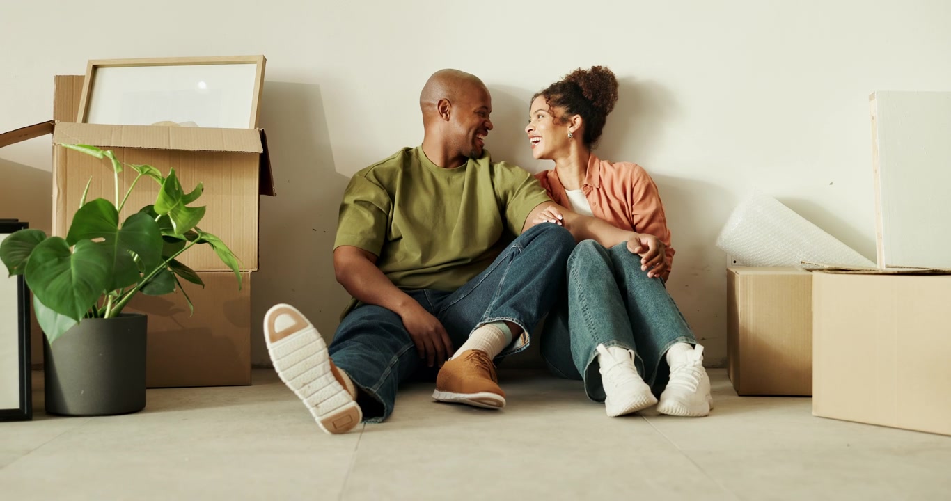Happy Couple Sitting on Floor in New Home Surrounded by Moving Boxes