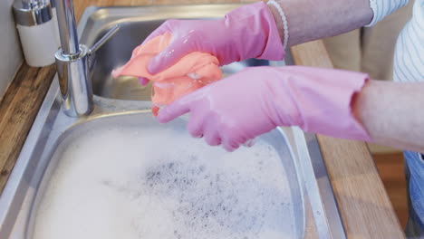 middle aged hands of caucasian woman washing up in gloves in kitchen with copy space