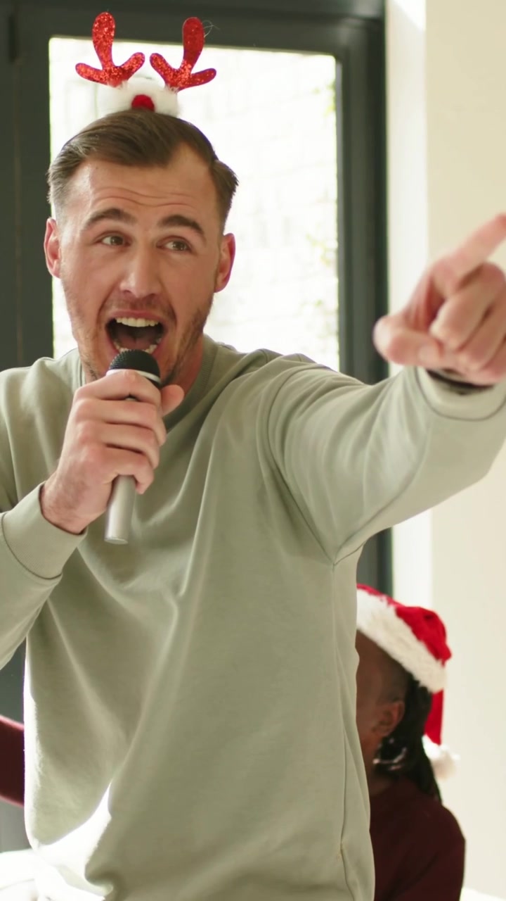 Video verticale: Iniziando una canzone, donna che passa il microfono a una festa a casa, uomo che canta con corna di renna e microfono