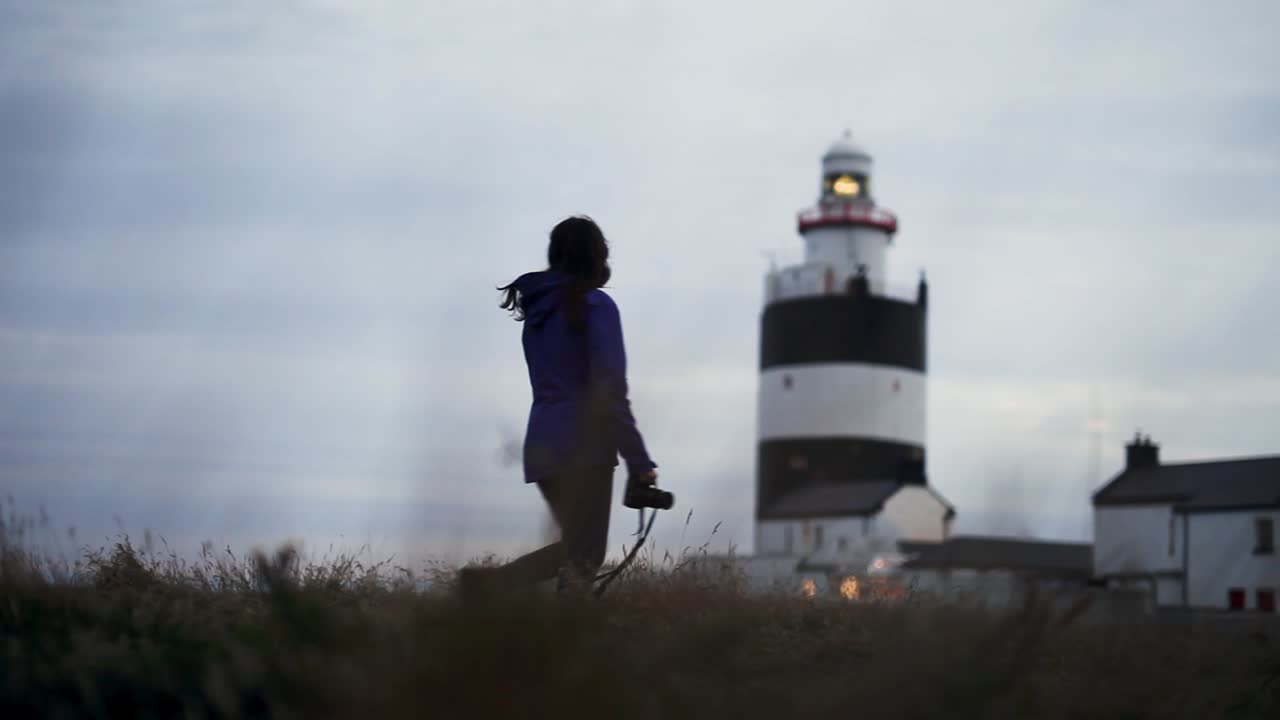 joven fotógrafa caminando hacia el faro bajo un cielo nublado