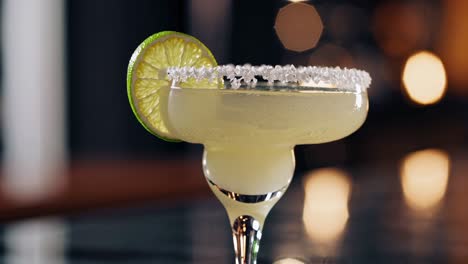 refreshing margarita cocktail garnished with lime and salt, placed on a bar counter with blurred background lights, creating a sophisticated and inviting atmosphere