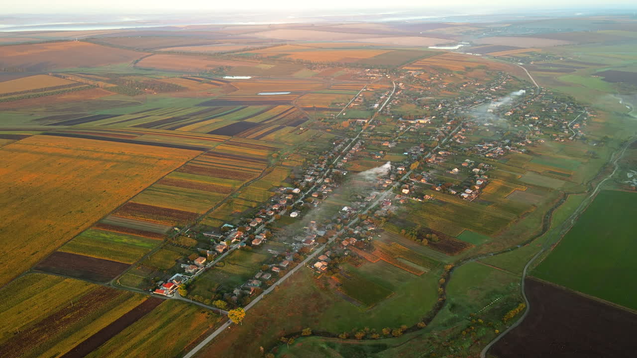 Aerial drone view of village in Moldova at sunset. Few columns of smoke from fires, wide fields
