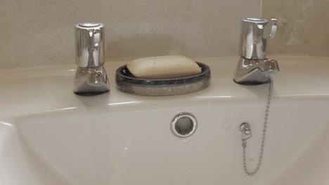 close up pan shot of sink wash basin with taps and soap against tiled wall