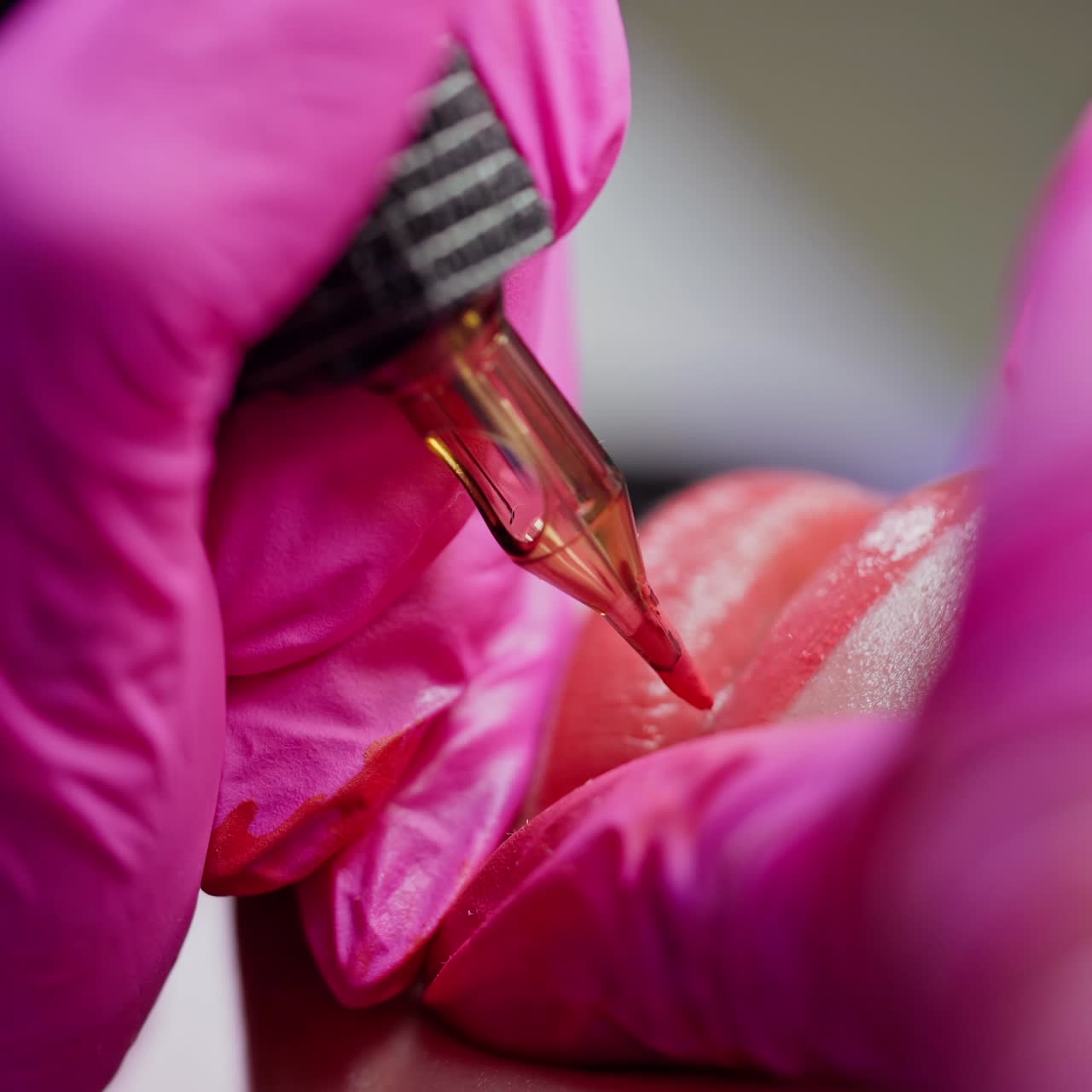 Permanent make-up on lips. Cosmetology procedure. Hands in pink gloves applying red permanent tattoo on girl's lips. Close-up.
