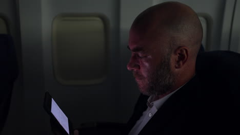 Un-Hombre-Viendo-Un-Vídeo-En-Una-Tableta-En-Un-Avión-De-Pasajeros-Por-La-Noche-En-Una-Cabina-Oscura