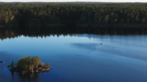 cinematic drone view of lake, island and boat surrounded by coniferous forest in sweden