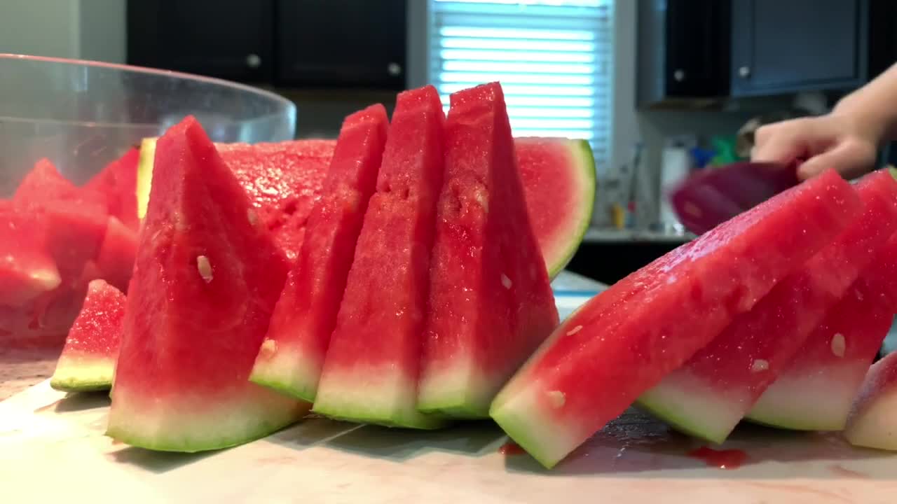 Hand slicing a fresh watermelon with a pink ceramic kitchen knife. 4K closeup video