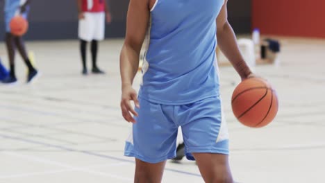 african american male basketball player bouncing ball, training at indoor court, slow motion