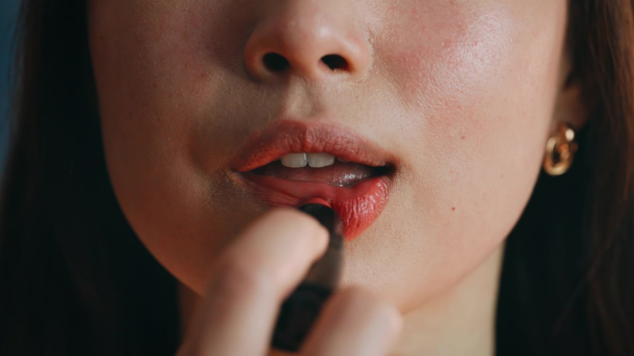 Closeup Asian woman applying coral lipstick. Macro lips makeup beauty routine.