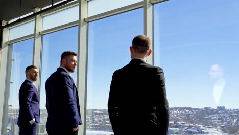 business people by the large office window. top managers in suits making an important decision while standing inside the office. panoramic window view on a city.
