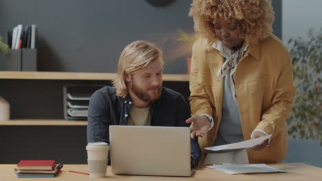 multiethnic coworkers using laptop and talking in office