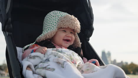 Adorable-mixed-race-Asian-baby-sitting-in-stroller-smiling-and-laughing-on-cold-sunny-winter-morning