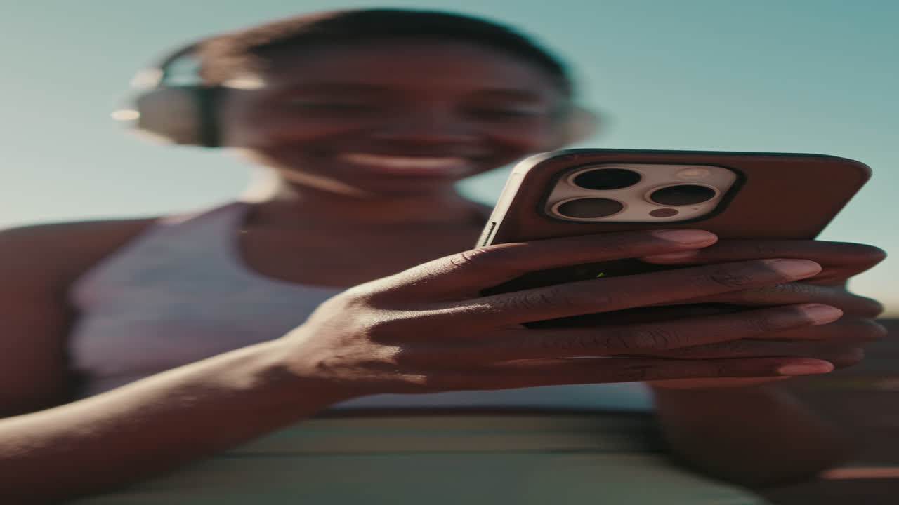 Giovane donna afroamericana con cuffie usa lo smartphone all'aperto