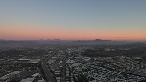 Eine-Schwenkdrohnenaufnahme-Fängt-Einen-Wunderschönen-Sonnenuntergang-über-Der-Stadt-Ein,-Wobei-Der-Mond-In-Der-Ferne-Sichtbar-Ist