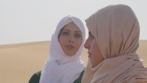 portrait of two muslim women wearing hijab standing in a windy desert