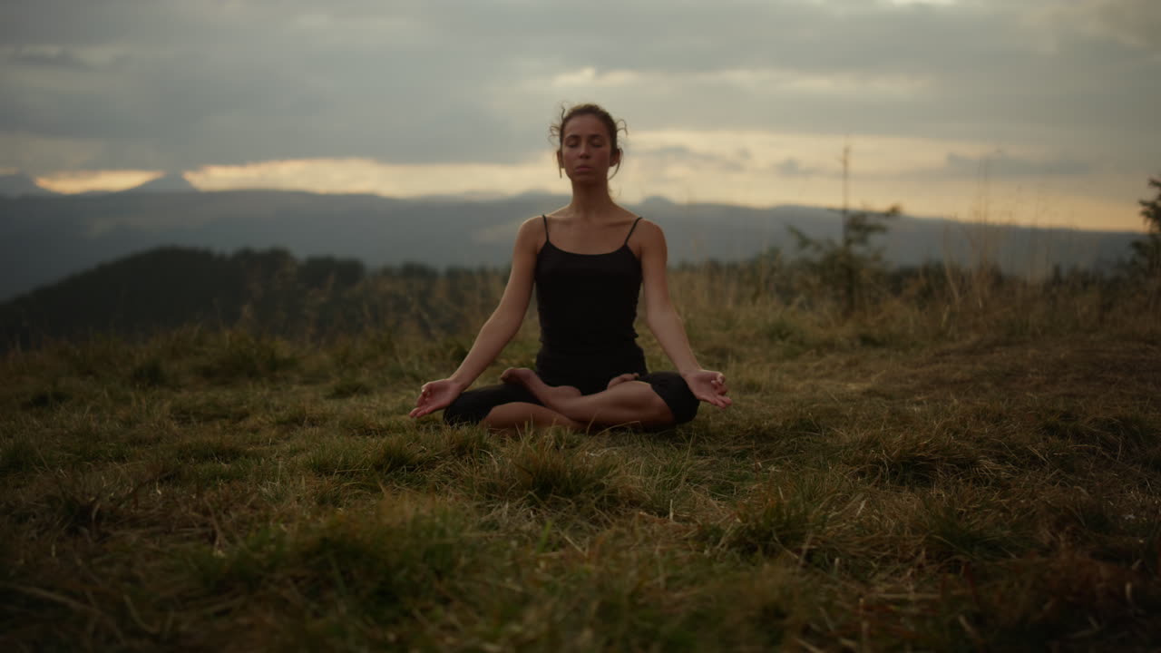 mujer seria sentada en pose de loto en la hierba. niña enfocada meditando al aire libre