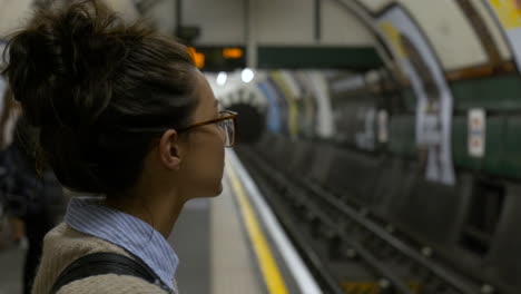 Woman-stood-on-underground-platform-waiting-for-tube-train,-London