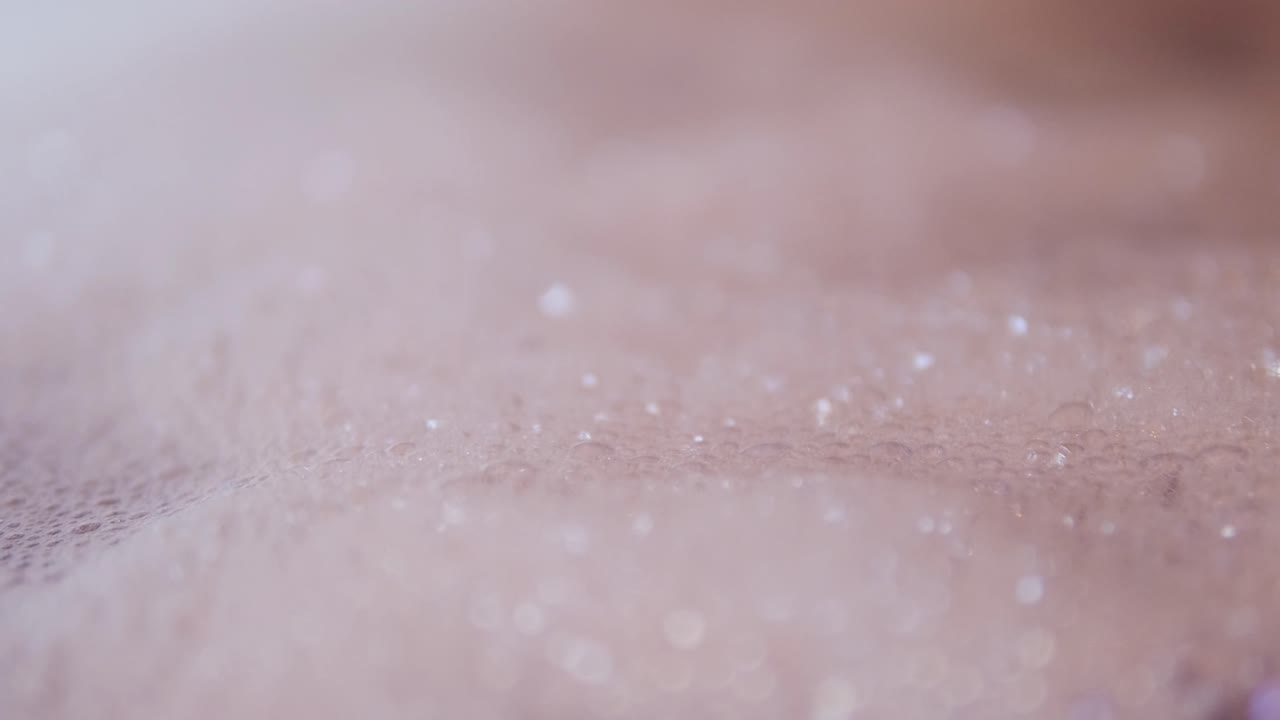 Close up view of foam and soapy bubbles on a moving water surface, self care, bathtub, pink background