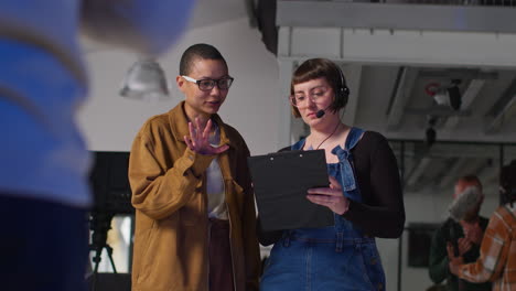 female film director and assistant watching actors and checking script shooting movie or video scene in studio 3