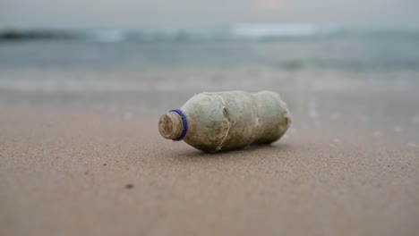 a plastic bottle lying on the beach with waves crashing in the backgrond