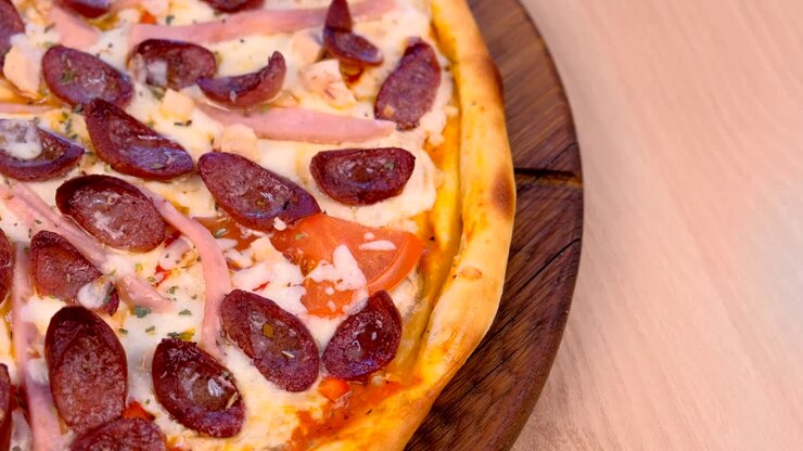 Spicchio di pizza con salsiccia affumicata, prosciutto e formaggio.